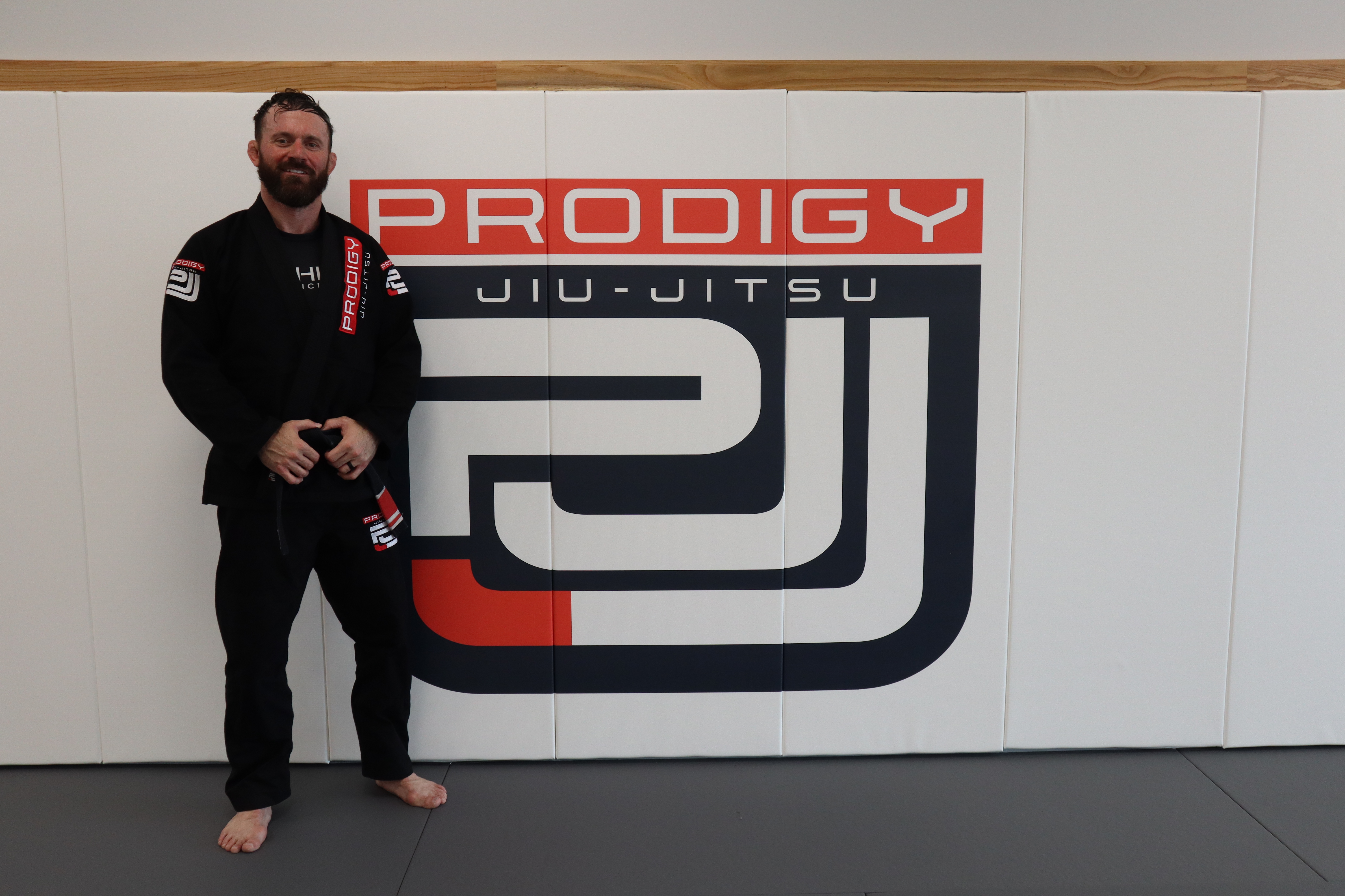 Coach Jeremy Lee Henderson — Head BJJ Instructor at Prodigy Jiu-Jitsu, standing in front of the academy logo