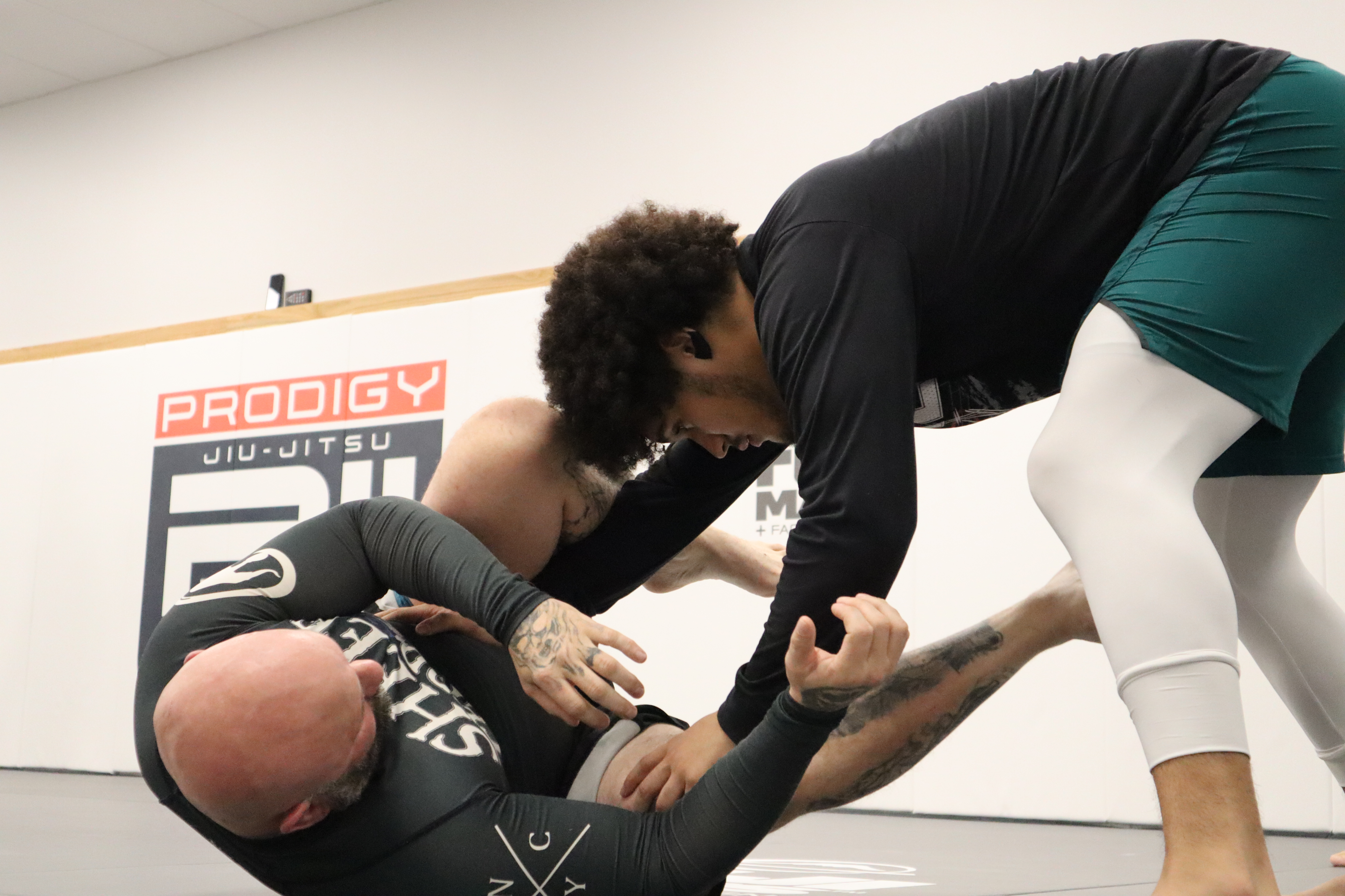 Adult students drilling No-Gi jiu-jitsu techniques at Prodigy Jiu-Jitsu with logo visible